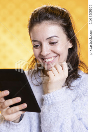 Woman amused by humorous ebook, conveying joy of reading concept, studio background. Geek enjoying comical digital novel on ereader screen, giggling at jokes, showing appreciation for literature Woman amused by humorous ebook, conveying joy of reading concept, studio background. Geek enjoying comical digital novel on ereader screen, giggling at jokes, showing appreciation for literature 116863993
