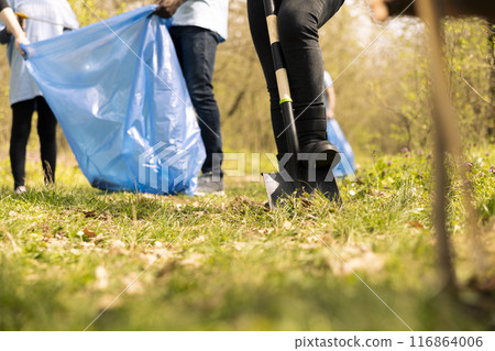 Team of activists clearing the forest area from rubbish and plastic, collecting garbage with tongs and bags. People doing voluntary work to preserve natural environment, illegal dumping. 116864006