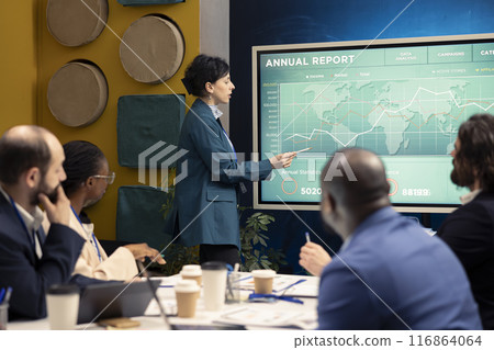 Marketing specialist showing infographics in a status update meeting, studying customer satisfaction and retention with annual data reports. Employee operating interactive board. Marketing specialist showing infographics in a status update meeting, studying customer satisfaction and retention with annual data reports. Employee operating interactive board. 116864064