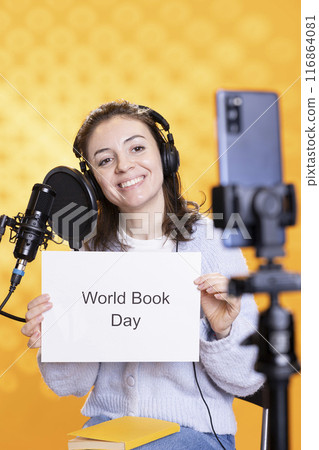 Smiling woman holding placard with world book day message written on it, filming with phone, studio background. Happy content creator recording video promoting importance of reading Smiling woman holding placard with world book day message written on it, filming with phone, studio background. Happy content creator recording video promoting importance of reading 116864081