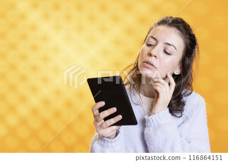 Woman reading textbooks on electronic ebook reader, gathering information for school exam, isolated over studio background. Student looking at digital books on tablet device display Woman reading textbooks on electronic ebook reader, gathering information for school exam, isolated over studio background. Student looking at digital books on tablet device display 116864151