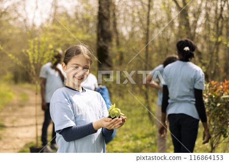 Cute little child getting ready to plant a small tree seedling in the forest, working to protect the natural environment and ecosystem. Young activist planting seeds to grow vegetation. 116864153