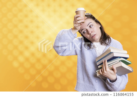 Woman feeling migraine from stress, carrying books for school exam and coffee cup to wake up, studio background. Exhausted student suffering headache from too much homework, drinking caffeine beverage Woman feeling migraine from stress, carrying books for school exam and coffee cup to wake up, studio background. Exhausted student suffering headache from too much homework, drinking caffeine beverage 116864155