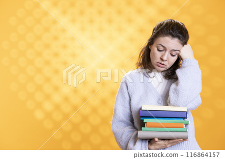 Portrait of upset woman holding pile of books, conveying hate of reading concept, isolated over studio background. Annoyed person with stack of novels showing disregard for literature Portrait of upset woman holding pile of books, conveying hate of reading concept, isolated over studio background. Annoyed person with stack of novels showing disregard for literature 116864157