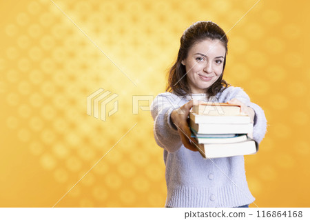 Portrait of friendly woman offering stack of textbooks useful for school exam, isolated over studio background. Merry person giving pile of books, recommending them for university assessment Portrait of friendly woman offering stack of textbooks useful for school exam, isolated over studio background. Merry person giving pile of books, recommending them for university assessment 116864168