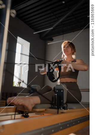 Woman training pilates on the reformer bed. Reformer pilates studio machine for fitness workouts in gym. Fit, healthy and strong authentical body. Fitness concept Woman training pilates on the reformer bed. Reformer pilates studio machine for fitness workouts in gym. Fit, healthy and strong authentical body. Fitness concept 116865669