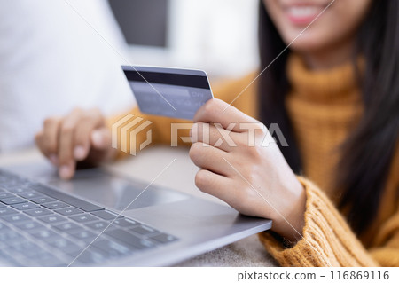 The woman uses her credit card to make online purchases, browsing various stores on her computer. The woman uses her credit card to make online purchases, browsing various stores on her computer. 116869116