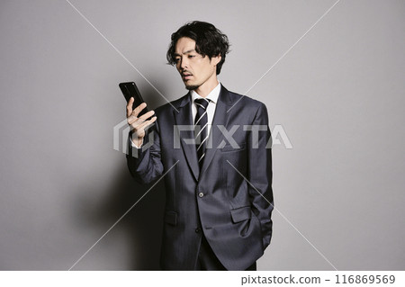 一個男人在灰色背景下看著智慧型手機 116869569