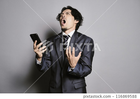 一個男人在灰色背景下看著智慧型手機 一個男人在灰色背景下看著智慧型手機 116869588
