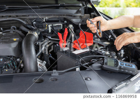 Senior Woman is jumping charger cable to AGM battery on car. 116869958