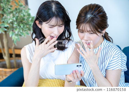 Two women watching videos on a smartphone Two women watching videos on a smartphone 116870158