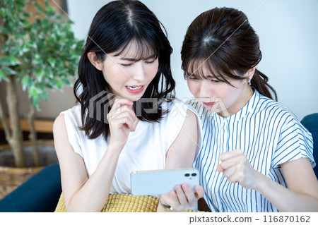 Two women watching videos on a smartphone 116870162