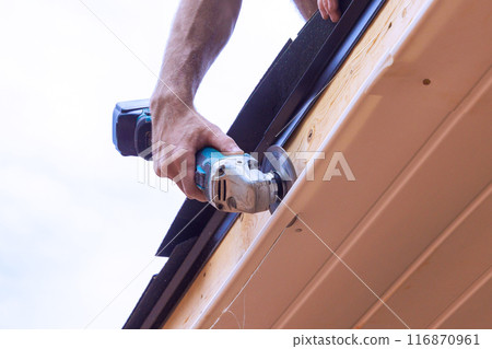 An employee cuts off vinyl soffit panels to given size on facade ceiling of new home 116870961