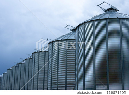 Minimal view to a row of gray metal granaries and sky. Minimal view to a row of gray metal granaries and sky. 116871305
