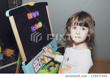 Toddler girl learning letters on the magnetic easel at home. Toddler girl learning letters on the magnetic easel at home. 116871448