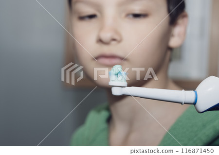 Boy in green bathrobe with an electric toothbrush and toothpaste in the bathroom. 116871450