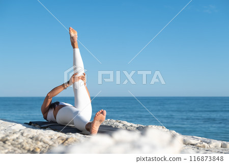 A woman in white sports clothes practices yoga exercises outdoors among white cliffs overlooking the sea A woman in white sports clothes practices yoga exercises outdoors among white cliffs overlooking the sea 116873848