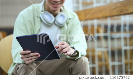 Young stylish man with headphone on neck using digital tablet at cafe Young stylish man with headphone on neck using digital tablet at cafe 116875762