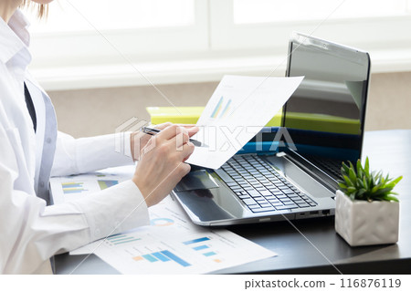 Business woman holding paper account documents, working at the table at the workplace with a laptop computer in the office indoors. The concept of working with financial documents 116876119