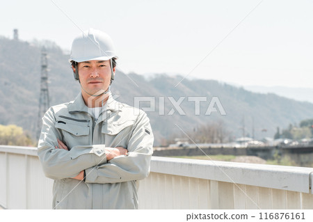 Asian male worker in work clothes with arms folded on a bridge (general contractor, construction manager, site supervisor) 116876161