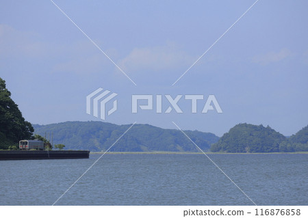 A local train with a red stripe on the Hanasaki Line running along Lake Akkeshi in Hokkaido on a calm, sunny summer day A local train with a red stripe on the Hanasaki Line running along Lake Akkeshi in Hokkaido on a calm, sunny summer day 116876858