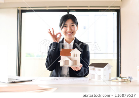 A businesswoman holding a house model and saying OK A businesswoman holding a house model and saying OK 116879527