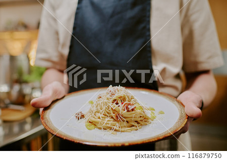 Medium close up of ceramic round plate with spaghetti carbonara covered with parmigiano, unrecognizable male hand holding plate Medium close up of ceramic round plate with spaghetti carbonara covered with parmigiano, unrecognizable male hand holding plate 116879750