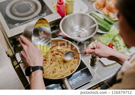 Top view of unrecognizable male hands holding steel bowls with three yolks and adding them into spaghetti carbonara 116879752