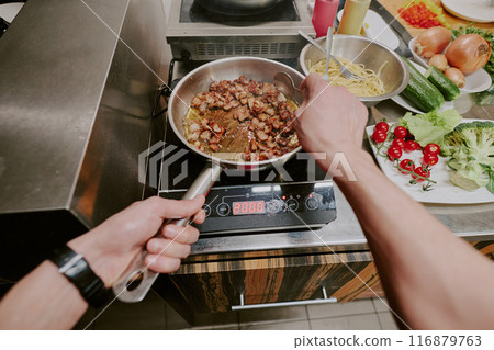 High angle shot of unrecognizable male hands holding pan and spoon while stirring bacon frying in pan High angle shot of unrecognizable male hands holding pan and spoon while stirring bacon frying in pan 116879763