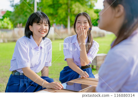 Asian school girls teen friend in school uniform talking leisure together happy laughing at park Asian school girls teen friend in school uniform talking leisure together happy laughing at park 116880314
