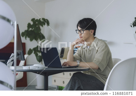 一名20多歲的男子戴著眼鏡在電腦上工作 一名20多歲的男子戴著眼鏡在電腦上工作 116881071