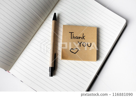 Sticky note with handwritten phrase thank you on a notebook with pen  top view 116881090