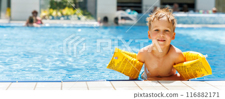 Portrait cute adorable little caucasian blond boy kid wear inflatable armband sit poolside indoor pool edge before swimming hotel spa thermal resort. Happy child enjoy summer vacation travel family Portrait cute adorable little caucasian blond boy kid wear inflatable armband sit poolside indoor pool edge before swimming hotel spa thermal resort. Happy child enjoy summer vacation travel family 116882171