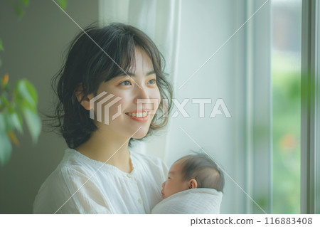 Young Asian woman holding her baby by the window in the living room. 116883408