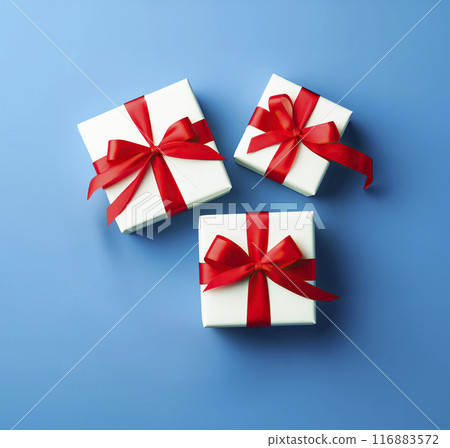 Three white gift boxes with red satin ribbons on a blue background. Gifts for Christmas, New Year, Valentine's Day, Birthday 116883572