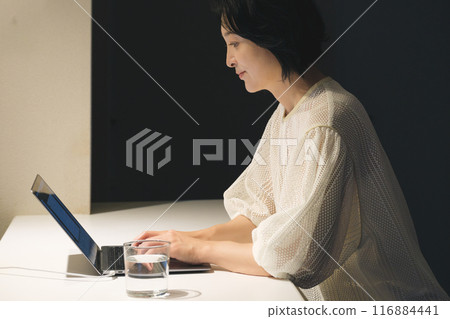 A middle-aged woman working at a computer at night 116884441