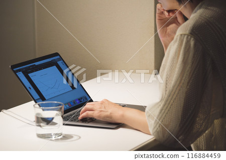 A middle-aged woman working at a computer at night 116884459