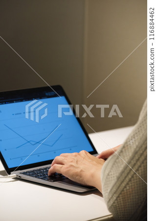 A middle-aged woman working at a computer at night 116884462