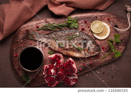 Fried dorado fish, with spices and herbs, on a wooden board, pomegranate sauce, close-up, no people, 116886585