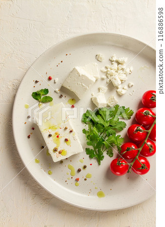 feta cheese, for salads, with cherry , green butter, greens, on a white plate, appetizer, top view, close-up, 116886598