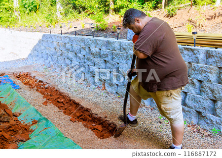 On construction site, worker digs trench to lay perforated pipe as part of drainage system. 116887172