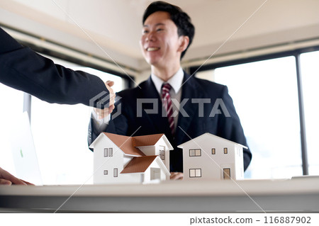 Male and female businessmen shaking hands in front of an architectural model Male and female businessmen shaking hands in front of an architectural model 116887902