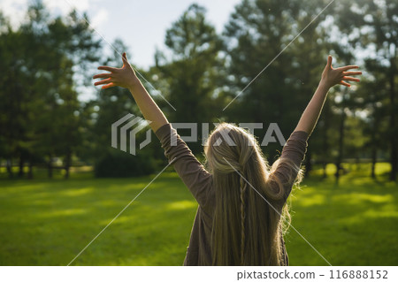female teen girl from behind standing in park with raised arms 116888152