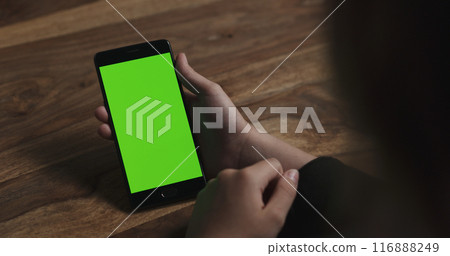 female teen girl holding smartphone with green screen sitting at the table female teen girl holding smartphone with green screen sitting at the table 116888249