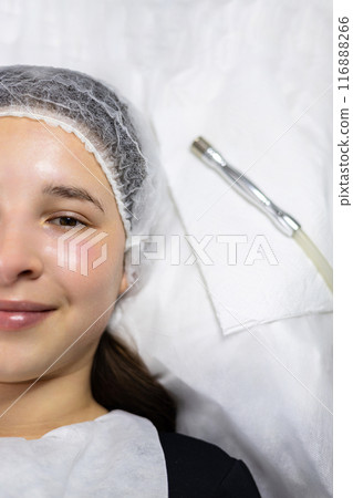 Close up, from above view, shot of a young woman after a beauty microdermabrasion procedure with derma pen, lying on the procedure table next to derma pen. Close up, from above view, shot of a young woman after a beauty microdermabrasion procedure with derma pen, lying on the procedure table next to derma pen. 116888266