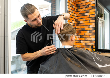 Haircut for little kid boy, professional barber doing haircut. Hairdress for children. Kid portraits in the barbershop 116888350