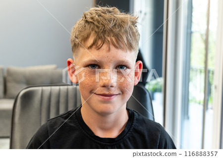 A picture of a very happy child after being cut in a barbshop salon, he has a very nice cut and has freckles on his face. 116888357