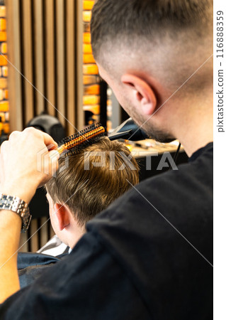 Picture of a process from a barbershop studio, how a child's hair is dried with a hair dryer and styled to be beautiful. 116888359