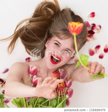Ecstatic lovely lady is posing with tulips for Woman's Day, with flowers nestled on her chest and in her hands. Expression smiling blonde woman beaming with joy as she lies down on white background 116888470