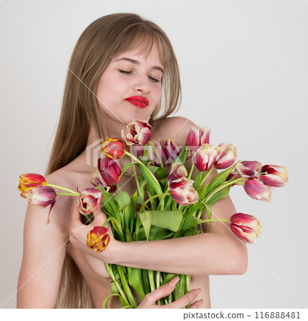 Portrait of beautiful young woman with her eyes closed holding bouquet of spring tulips in her hands and covering her lovely chest with them. Idea for festive International Mother's Day concept 116888481